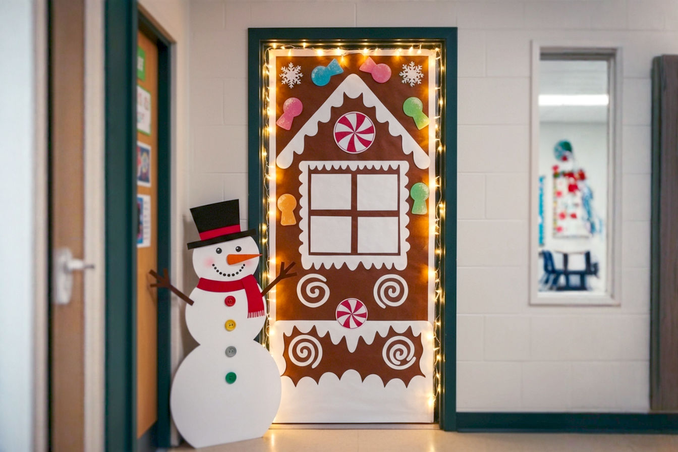 A vibrant, eye-level, professional photograph of a beautifully decorated classroom door for Christmas. The door is adorned with a cheerful, detailed "Gingerbread House" theme, featuring brown paper "gingerbread" walls, white "icing" swirls, and colorful "candy" cutouts (gumdrops, peppermints). A large, friendly paper snowman with a carrot nose and button eyes stands slightly to the side of the door. The scene is brightly lit with soft, warm, battery-operated LED fairy lights woven around the door frame and within the decorations, creating a magical glow. The composition is a wide shot, capturing the full door and a hint of the festive classroom hallway in the background, out of focus. The lighting is soft and inviting, emphasizing the textures and colors of the decorations. The mood is joyful, whimsical, and welcoming, with a strong sense of holiday spirit. Lifelike, high-resolution, pro photography style.