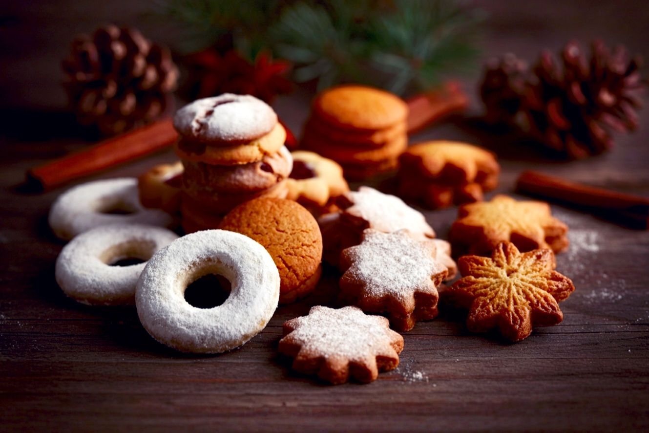 Pro photography style, lifelike, warm, inviting scene of a variety of traditional German Christmas cookies artfully arranged on a rustic wooden table. Include iconic cookies like Lebkuchen, Zimtsterne, Spritzgebäck, and Vanillekipferl, each perfectly baked and decorated. Soft, warm ambient lighting from a nearby window or fireplace, casting gentle shadows. A few subtle holiday decorations like pinecones, cinnamon sticks, or a sprig of evergreen are in the soft-focus background. The mood is cozy, festive, and nostalgic, emphasizing the rich textures and appealing colors of the cookies. Focus on a shallow depth of field, making the cookies pop. High-resolution, professional studio shot.