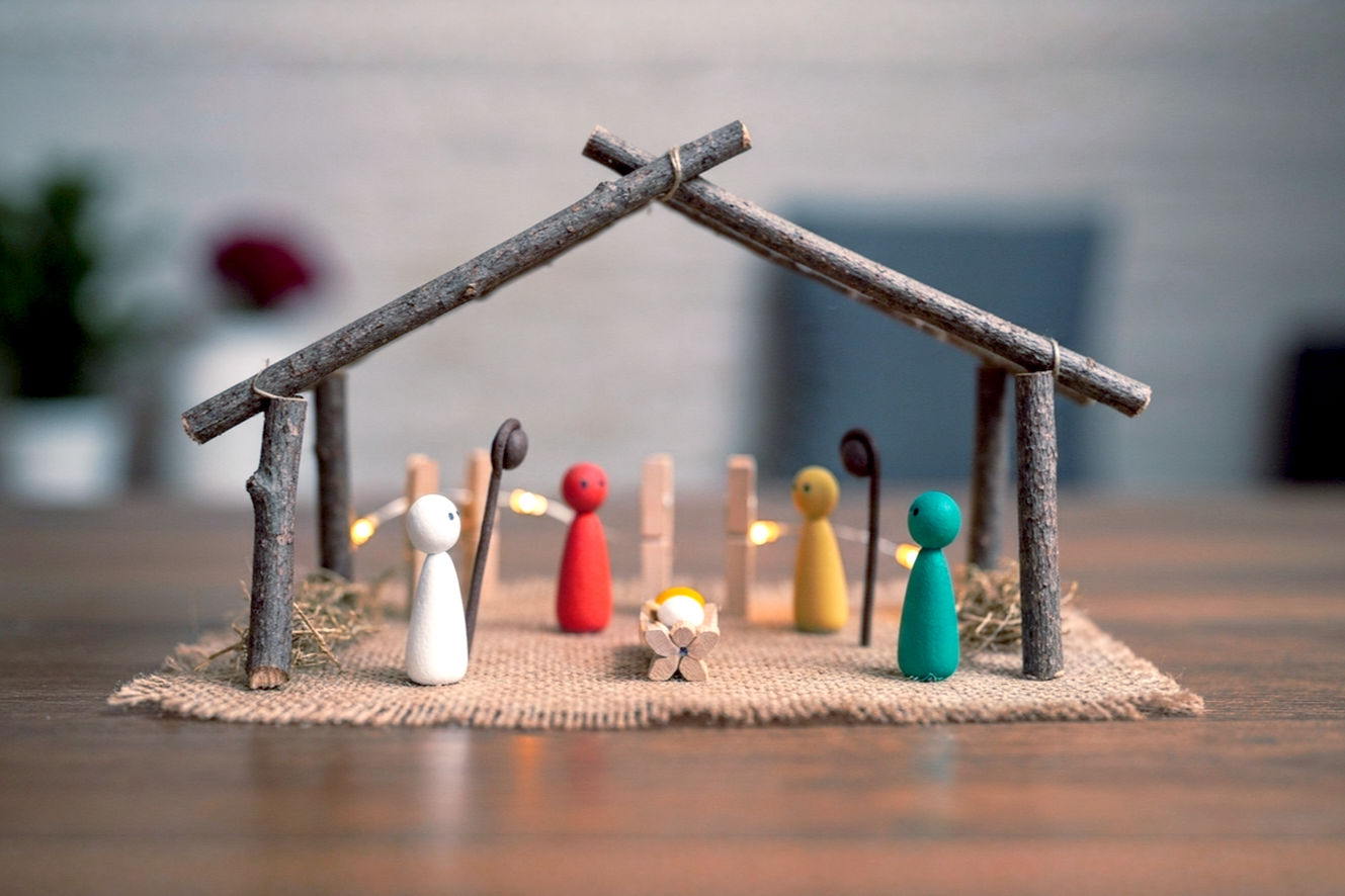 Professional, lifelike, high-resolution photography of a beautifully crafted, yet clearly simple and homemade, nativity scene. The scene should be composed of natural, rustic materials like twigs, burlap, and perhaps painted pebbles or clothespin figures, subtly hinting at its quick creation. The composition should be warm and inviting, with soft, ambient lighting (perhaps a subtle glow from within the stable, mimicking fairy lights). The background is gently blurred, suggesting a cozy, festive home environment. The overall mood is peaceful, reflective, and conveys the profound meaning of the holiday season, while also subtly suggesting the accessibility and ease of creation. Emphasize natural textures and a sense of handmade charm.