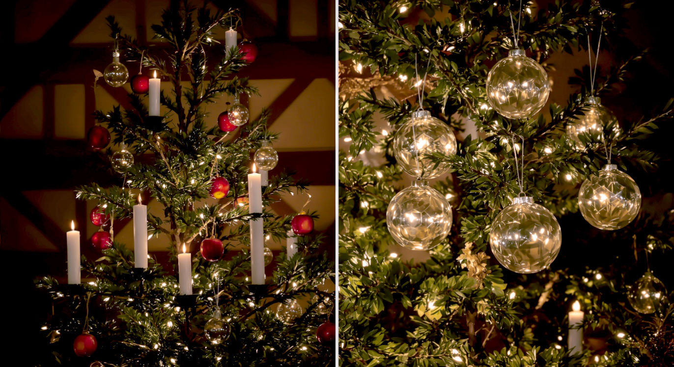 A detailed, professional photograph capturing the transition of Christmas decorations. In a rustic, 16th-century German room with a timber-frame wall, a candlelit Christmas tree is visible. On one side, the branches are sparsely decorated with natural elements like red apples and white candles. On the other side, the branches feature the first hand-blown glass kugels from Lauscha, shimmering with an inner silver lining. The composition should be a close-up, split-shot to highlight the contrast between the organic and the artisan. The lighting is low and warm, primarily from the candles, creating a nostalgic, historical, and slightly magical mood that evokes the birth of a tradition.